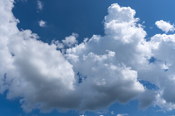 White cotton like puffy cumulus clouds against a blue sky with the suns rays shining.