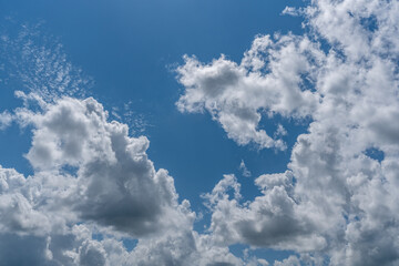 White cotton like puffy cumulus clouds against a blue sky with the suns rays shining.