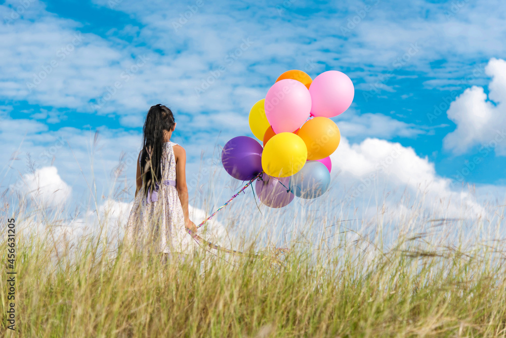 Wall mural cheerful cute girl holding balloons running on green meadow white cloud and blue sky with happiness.