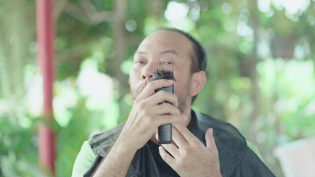 Man cutting a beard and mustach by himself at home with a hair clipper. Asian stay home and live during lockdown