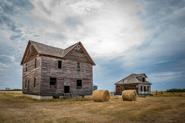 Two abandoned homes, hay bales and a classic car in the ghost town of Robsart, Saskatchewan