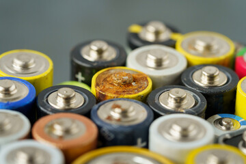 Close up of used battery with traces of rust and corrosion, selective soft focus. Lot of AA batteries over grey background. Electronic hazardous waste, recycling concept 