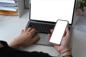 Young man using laptop computer and holding smart phone.