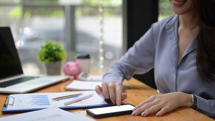 Smiling businesswoman sitting at her office desk and using mobile phone.