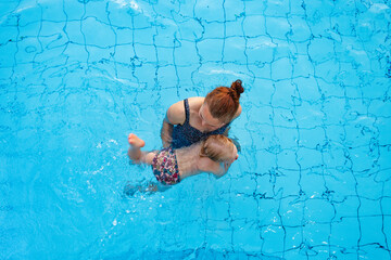 Happy family. Mom teaches her daughter 2-3 years old to swim in the pool. Top view.