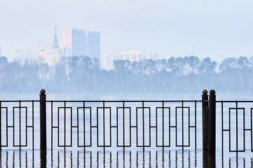 The fence of the city embankment during flooding with water and fog. Blur the background. Selective focus.