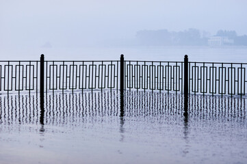 The fence of the city embankment during flooding with water and fog.