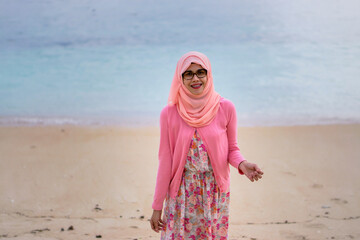 Portrait of beautiful young Asian muslim woman wearing pink dress and hijab standing by tropical...