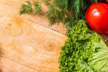 Lettuce, dill and tomato on a wooden background, top view.