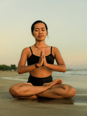 Fototapeta na wymiar Yoga retreat. Asian woman practicing Lotus pose. Padmasana. Hands in namaste mudra. Closed eyes. Healthy lifestyle. Yoga on the beach. Fit body. Seminyak beach, Bali, Indonesia