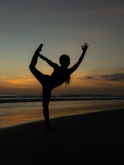 Yoga silhouette. Sunset beach yoga. Slim woman practicing standing asana Natarajasana, Lord of the Dance Pose. Balancing, back bending asana. Copy space. Seminyak beach, Bali