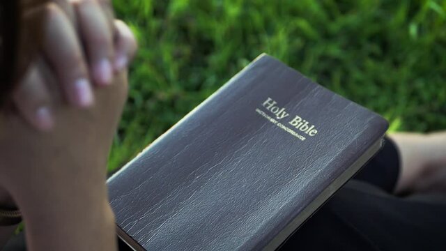 A woman prays with her hands across the Bible for God's blessing in the calm of nature.