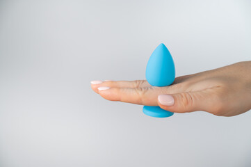 Woman holding a blue butt plug on a white background. Adult toy for alternative sex