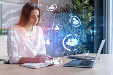 Attractive businesswoman in white shirt at workplace working with laptop to hire new employees for international business consulting. HR, social media hologram icons over office background