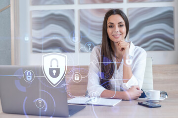 Attractive businesswoman in white shirt at workplace working with laptop to defend customer cyber security. Concept of clients information protection. Padlock hologram over office background.