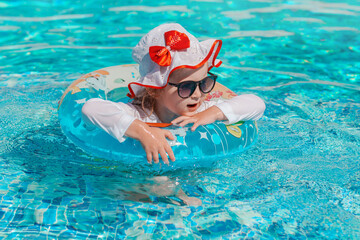 Fototapeta na wymiar Little girl swimming in pool in swimwear with sun protection and sunglasses. Healthy and safe summer outdoor activities.