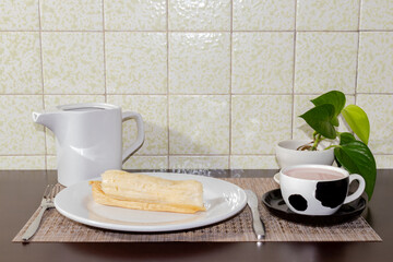 tamal de queso con atole de chocolate decoración planta verde con mesa cafe mantel cafe y cubiertos cuchillo tenedor planto blanco típico desayuno mexicano