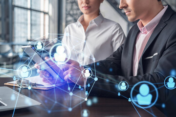 Businessman and businesswoman in formal wear working together looking for new employees to hire for international business consulting. HR, social media icons over modern panoramic office background