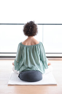 Caucasian woman with short curly hair sited in a yoga lotus pose