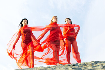 Naklejka premium Three girls with red transparent cloth on the top of sand dune, against blue sky