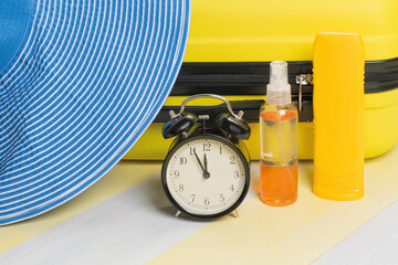 time to rest: travel suitcase, blue hat and sun protection on a yellow-gray background