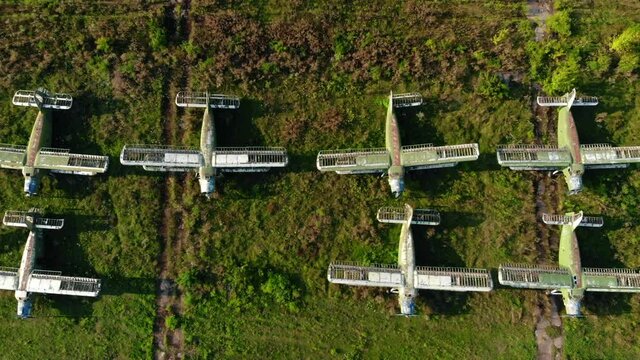 Large group of destroyed Antonov-2 and Antonov-24 airplanes stands on green grass airfield at abandoned military air base bird eye view