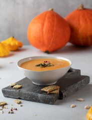 Pumpkin cream soup with seeds on a wooden board against the background of pumpkins. Autumn dish.