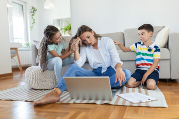 Small mischievous kids noising and distracting mother freelancer trying to concentrate on laptop...