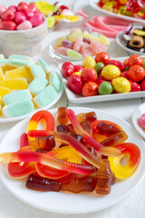 Different colorful flavored fruit candy on plates on a white wooden background. Vertical view