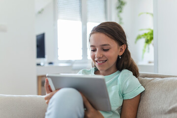 cute little happy girl smile sitting down on sofa using looking digital tablet pad in the living room at home. family activity concept.