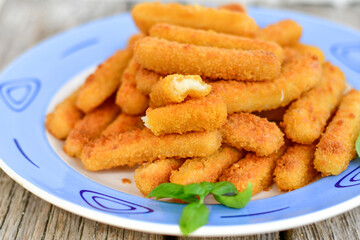 Vegetarian cheese breaded  oven baked  mozzarella sticks with  fresh basil on wooden background 