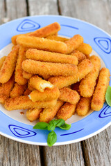 Vegetarian cheese breaded  oven baked  mozzarella sticks with  fresh basil on wooden background 