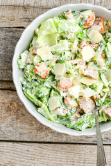 Homemade traditional Caesar Salad with Parmesan Cheese and Croutons in a white bowl on a old white table with leaves and a sauce boat 
