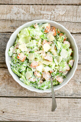 Homemade traditional Caesar Salad with Parmesan Cheese and Croutons in a white bowl on a old white table with leaves and a sauce boat 