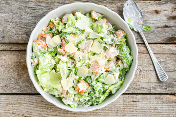 Homemade traditional Caesar Salad with Parmesan Cheese and Croutons in a white bowl on a old white table with leaves and a sauce boat 