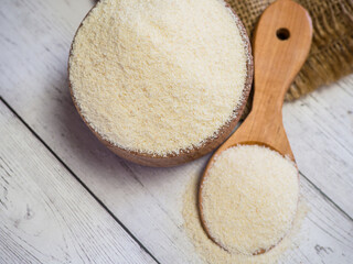 Semolina in a wooden bowl and spoon on a white wooden table, close-up. healthy diet cereals background.
