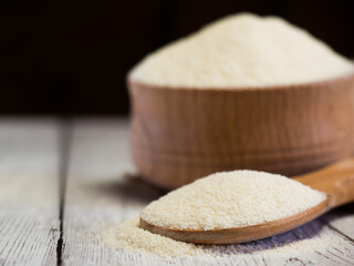Semolina in a wooden bowl and spoon on a white wooden table, close-up. healthy diet cereals background.