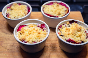 plums under the crumble in small white bowls placed on a wooden chopping board