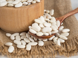 Fototapeta na wymiar white beans in a wooden spoon on a white wooden table, copy space