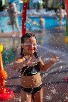 Child plays with the spray of water attraction. Little girl in swimsuit with watermelon image and glasses plays by pool during summer holidays. 