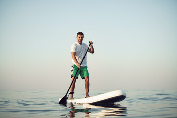 Young man in t-shirt and shorts floating on SUP board