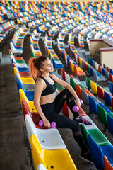 beautiful sporty woman coach doing exercises with colored chairs in the stadium
