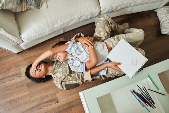 Funny boy closed eyes of his lovely mother wearing military uniform while laying