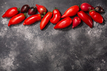 Ripe pepperlike heirloom tomatoes atop dark textured backdrop, copy spce, top view (Solanum lycopersicum fruits)