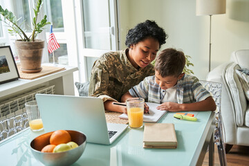 Woman wearing military jacket talking with her little son while sitting at the table with him
