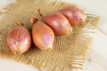 Group of four whole shallot on natural sackcloth on white wood