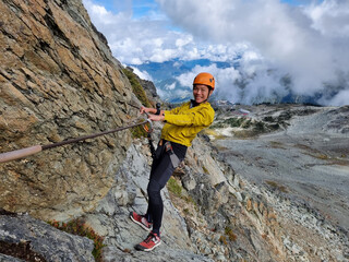 Via Ferrata climbing guided tour excursion happy Asian woman tourist hanging from rope at high pass...