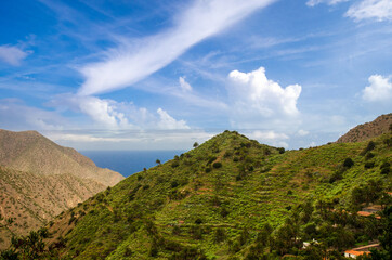 Wide angle shot of beautiful coastline on the Canary island of La Gomera in spring with seashore, mountains, vegetation, sky, clouds and sun; Spain in Europe