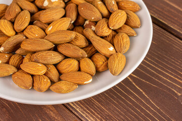 Lot of whole almond on white ceramic plate on brown wood