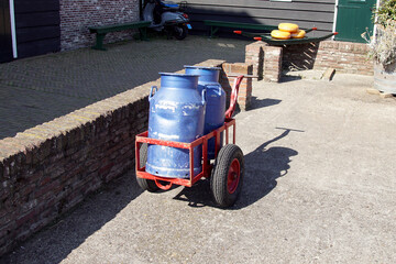 Fototapeta na wymiar Dutch red cart with blue painted, old milk cans on a farm yard. Small berrie with three round cheeses on the background. Summer, September, Netherlands.